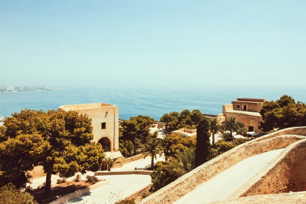 A sunny coastal city in Spain with sandy beaches and palm trees, ideal for US military retirees living overseas enjoying a relaxed Mediterranean retirement lifestyle.