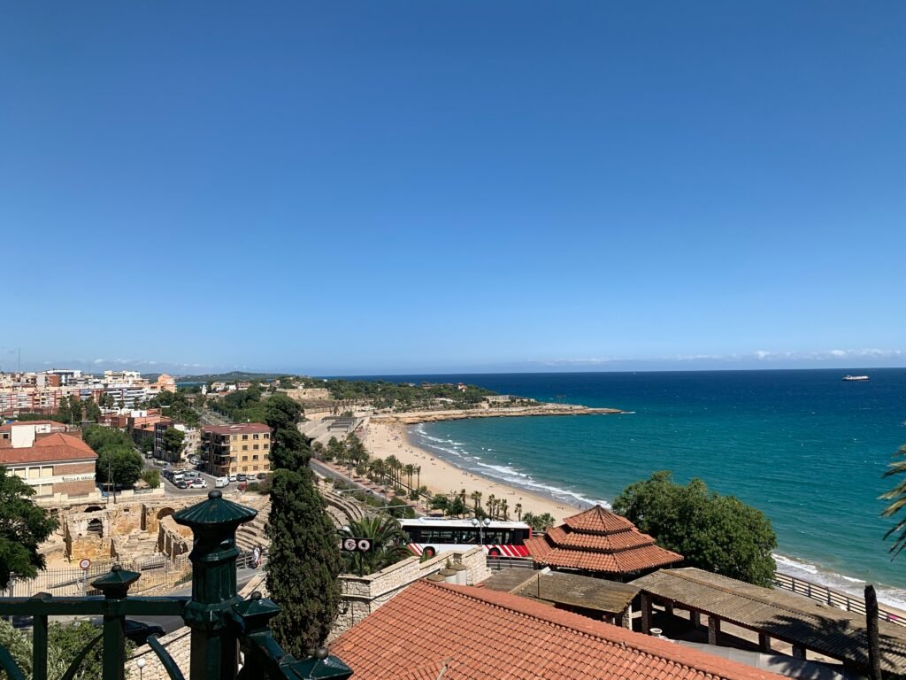  A panoramic shot of Tarragona’s coastline, showing its Roman amphitheater near the beach, golden sand, and the deep blue Mediterranean Sea.