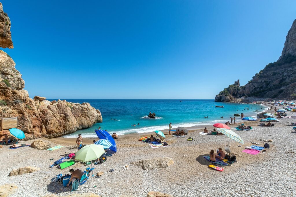 A beautiful Spanish beach with crystal-clear blue waters, golden sand, and sunbathers enjoying the Mediterranean coast, symbolizing the best places to live in Spain by the sea